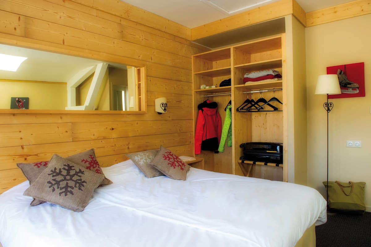 Ein Zimmer mit Holzboden, einem Bett, einem Spiegel, einem Kleiderschrank und einem Kleiderständer.