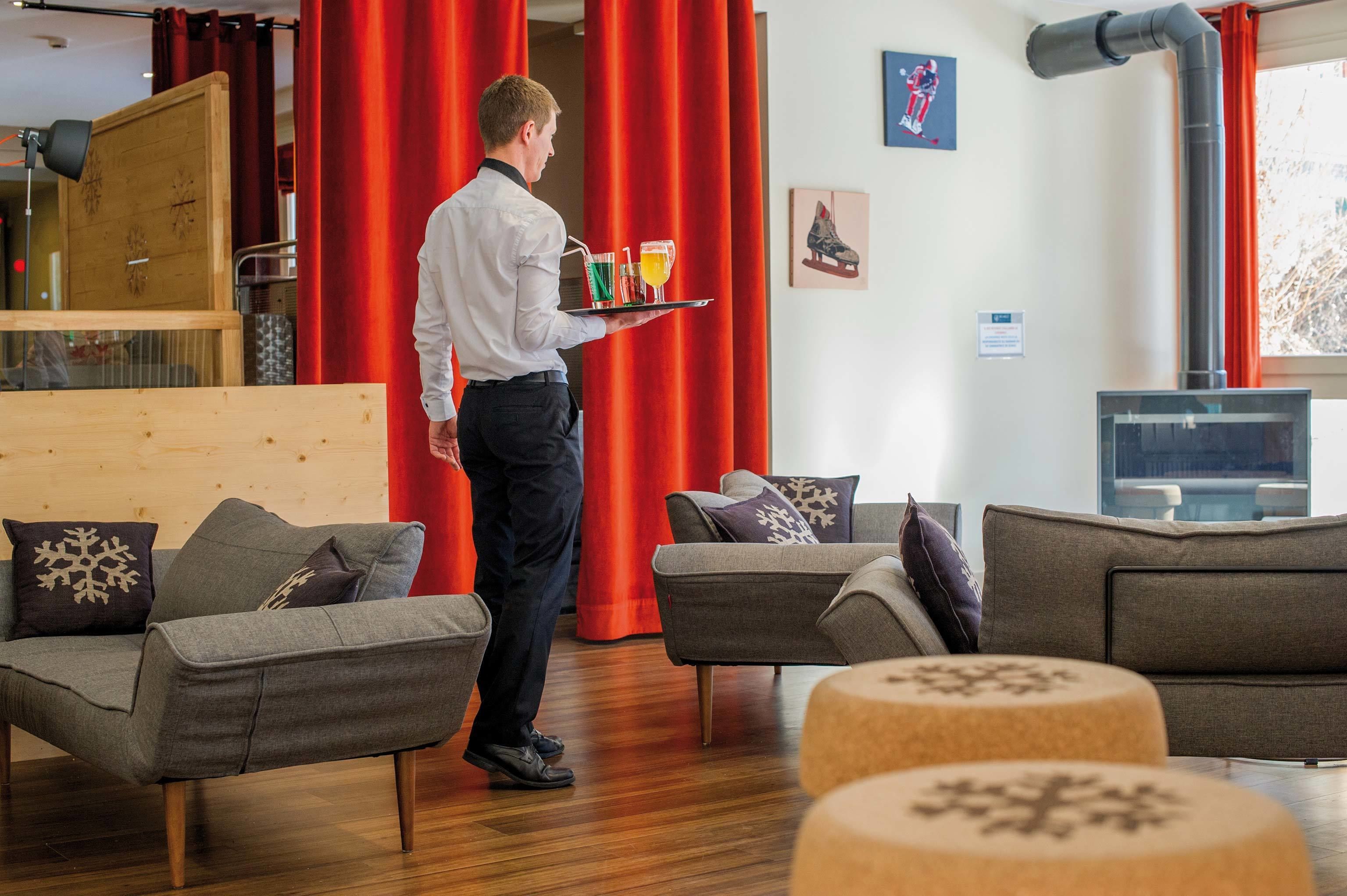 Un hall d’hôtel moderne avec des canapés gris, des rideaux rouges et un mur lambrissé.