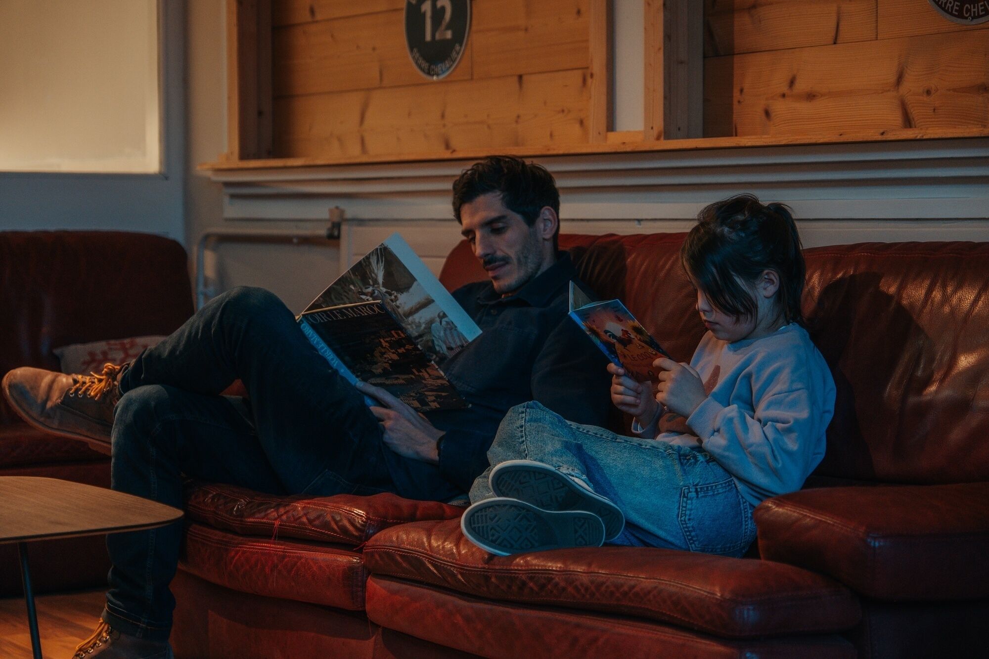 Un uomo e un bambino seduti su un divano in pelle che leggono libri.
