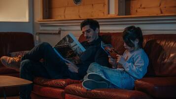 Un uomo e un bambino seduti su un divano in pelle che leggono libri.