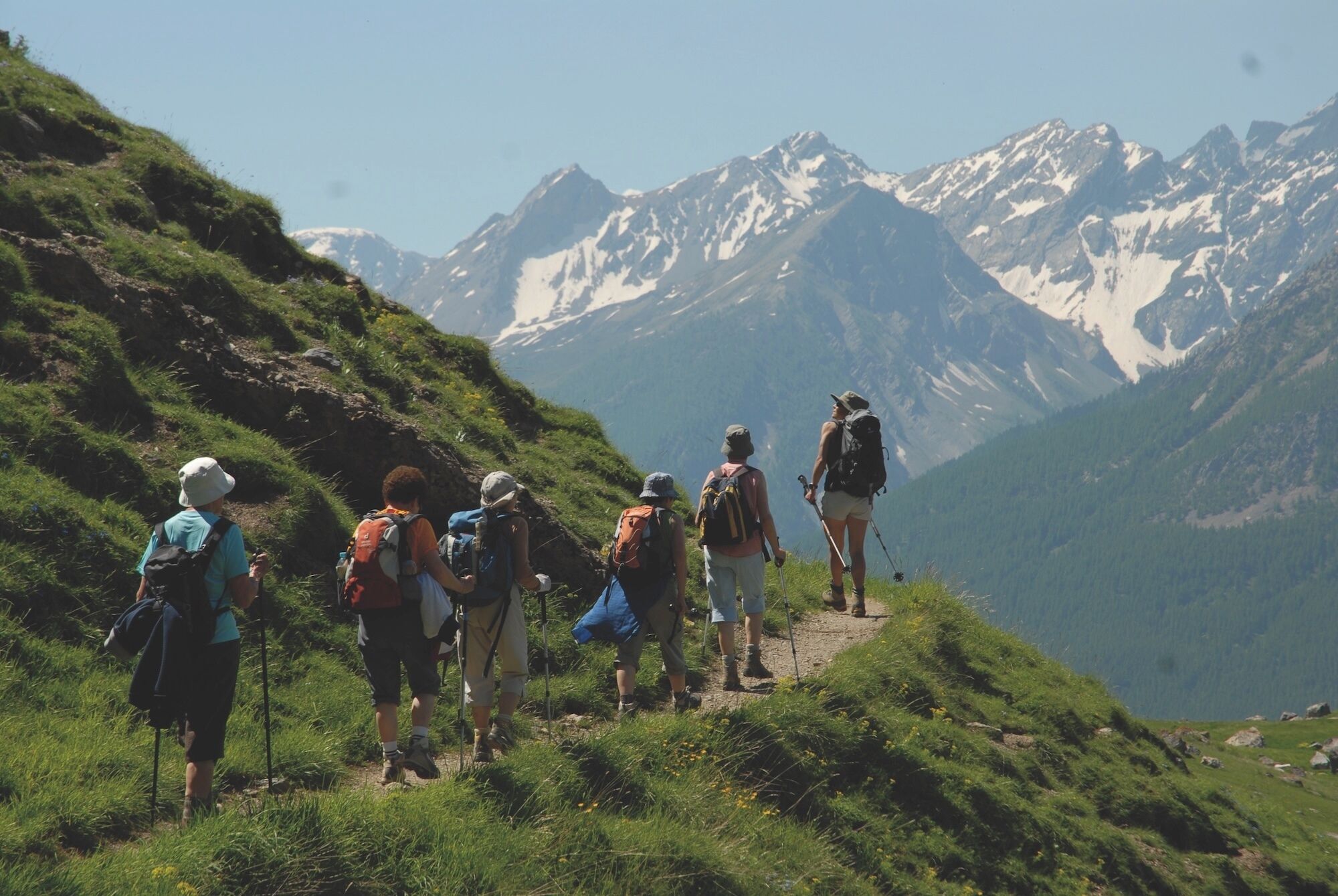 A group of hikers on a mountain trail with snow-capped peaks in the background.