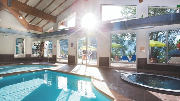 An indoor swimming pool with clear glass walls, a sunlit ceiling, and a view of the outside patio area. - Club Vacances Bleues Les Alpes d'Azur (La Salle-les-Alpes)