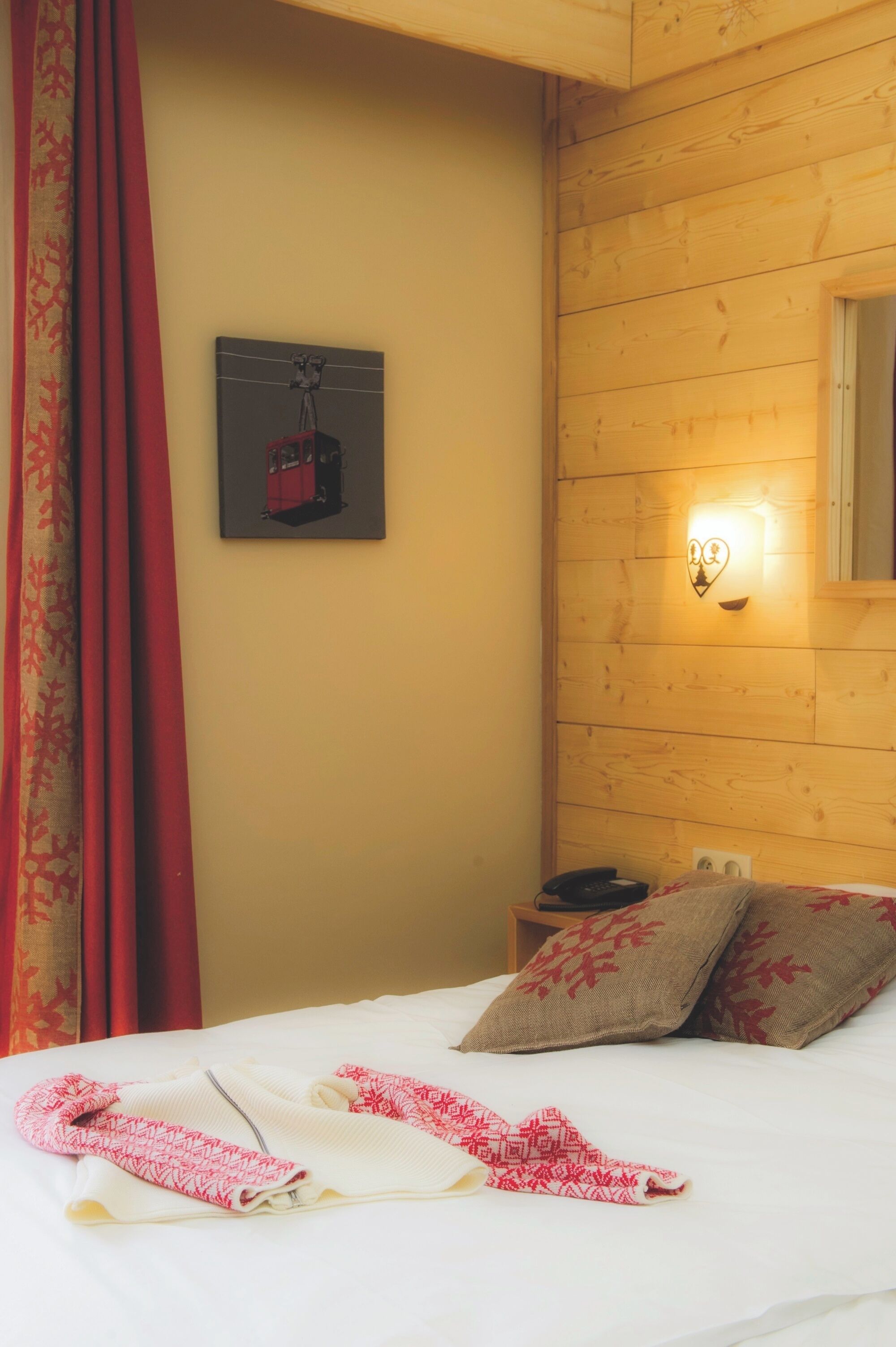 A hotel room with a bed, pillows, a nightstand, a wall-mounted light, and a framed picture.