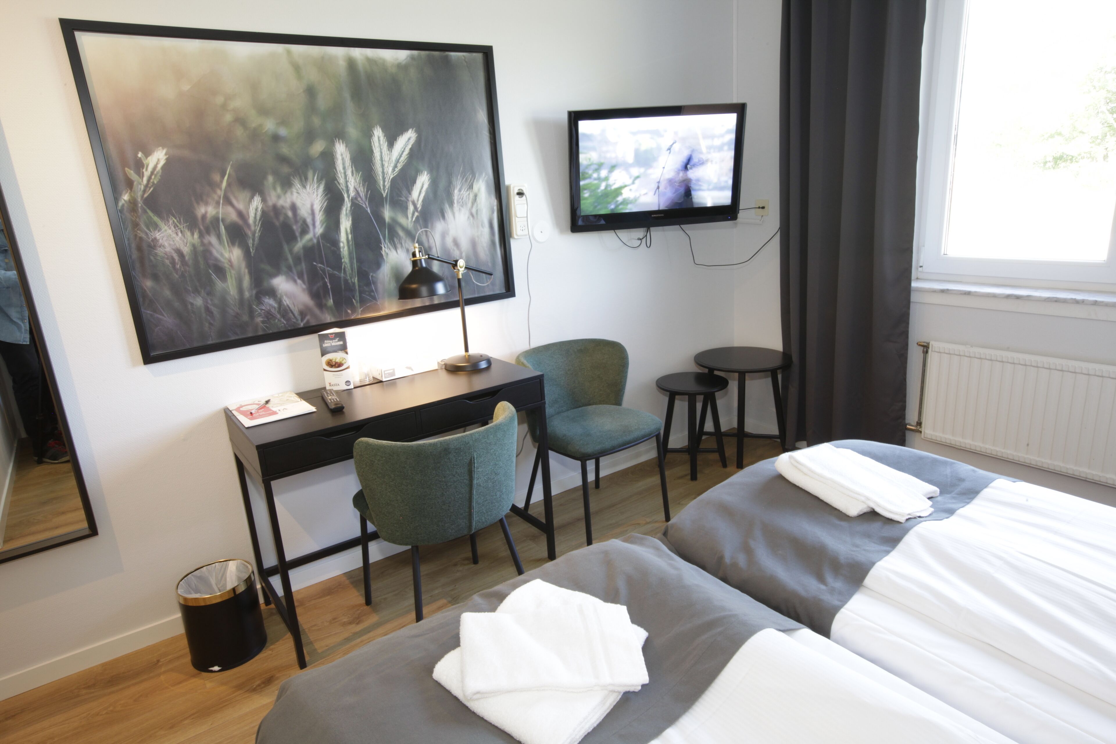 A hotel room with two beds, a desk, a chair, a TV, and a large painting on the wall.