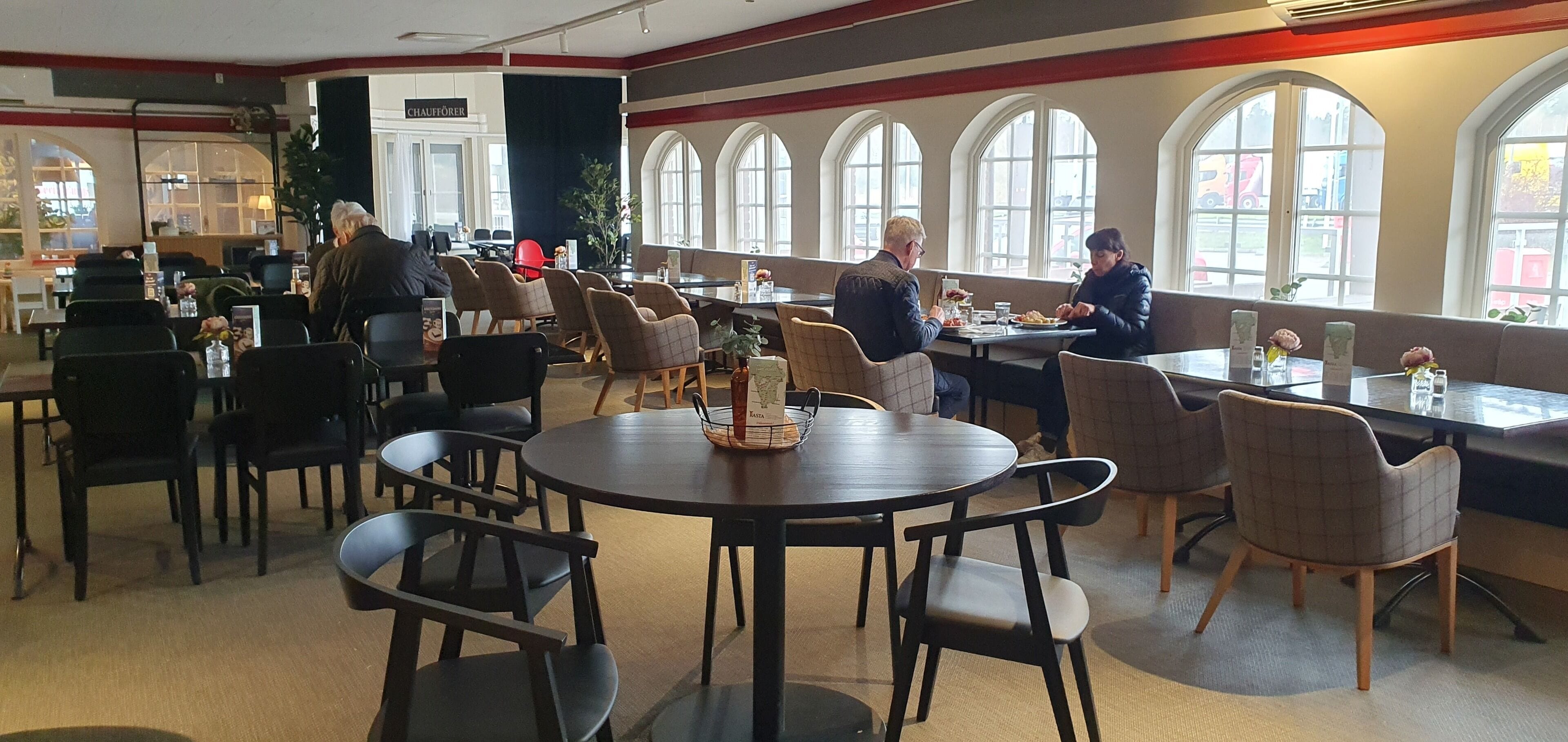 A restaurant with round tables and chairs, large windows, and a view of the street outside.