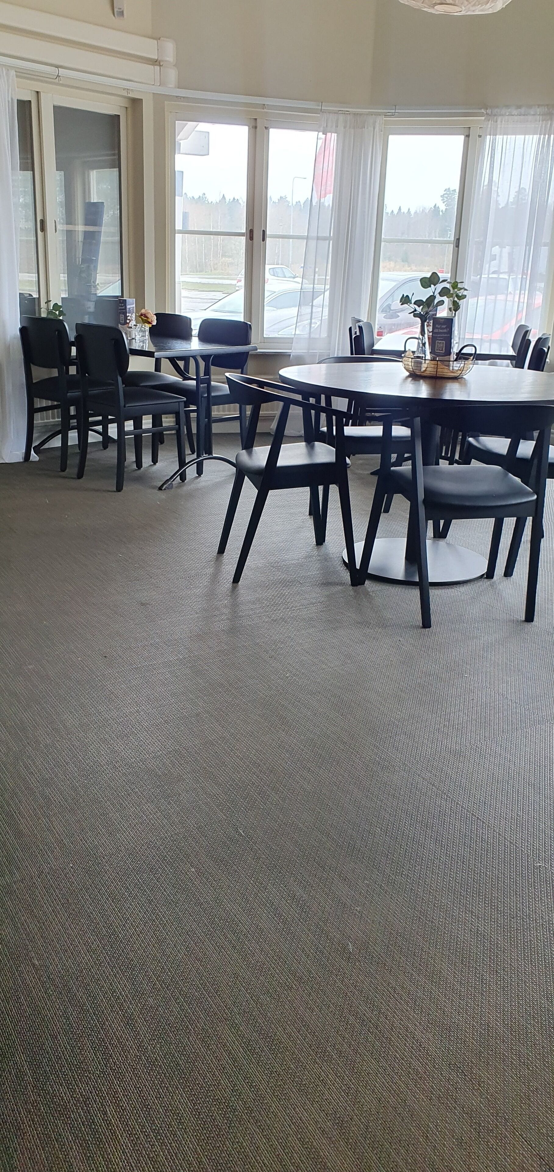 A conference room with a large table and multiple chairs, large windows with curtains, and a carpeted floor.