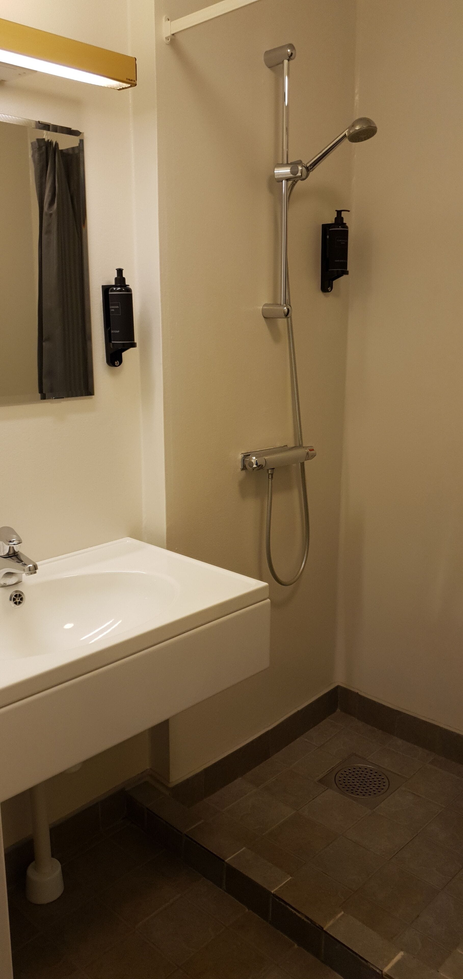 A bathroom with a white sink, a mirror, a shower with a handheld showerhead, and a handheld soap dispenser.