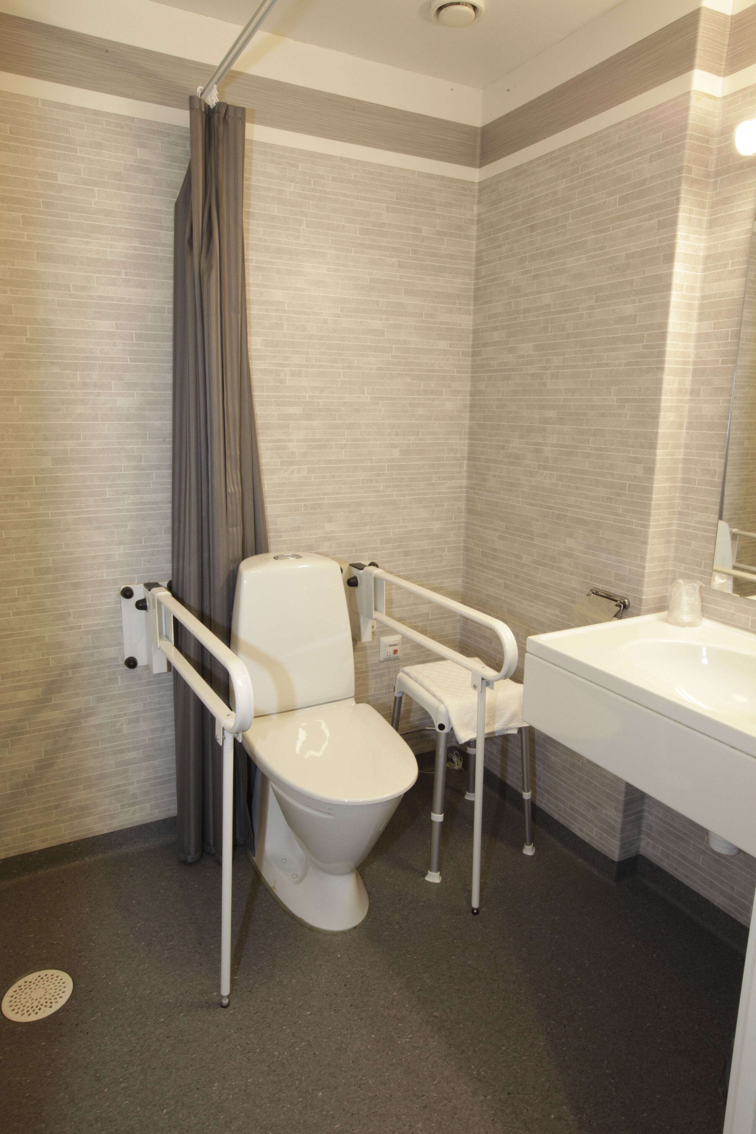 A modern bathroom with a wheelchair-accessible toilet, a shower with a curtain, and a sink with a mirror.