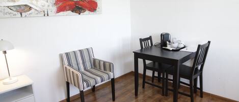 Un comedor con una mesa y sillas de madera, una silla a rayas, una lámpara y un cuadro en la pared.