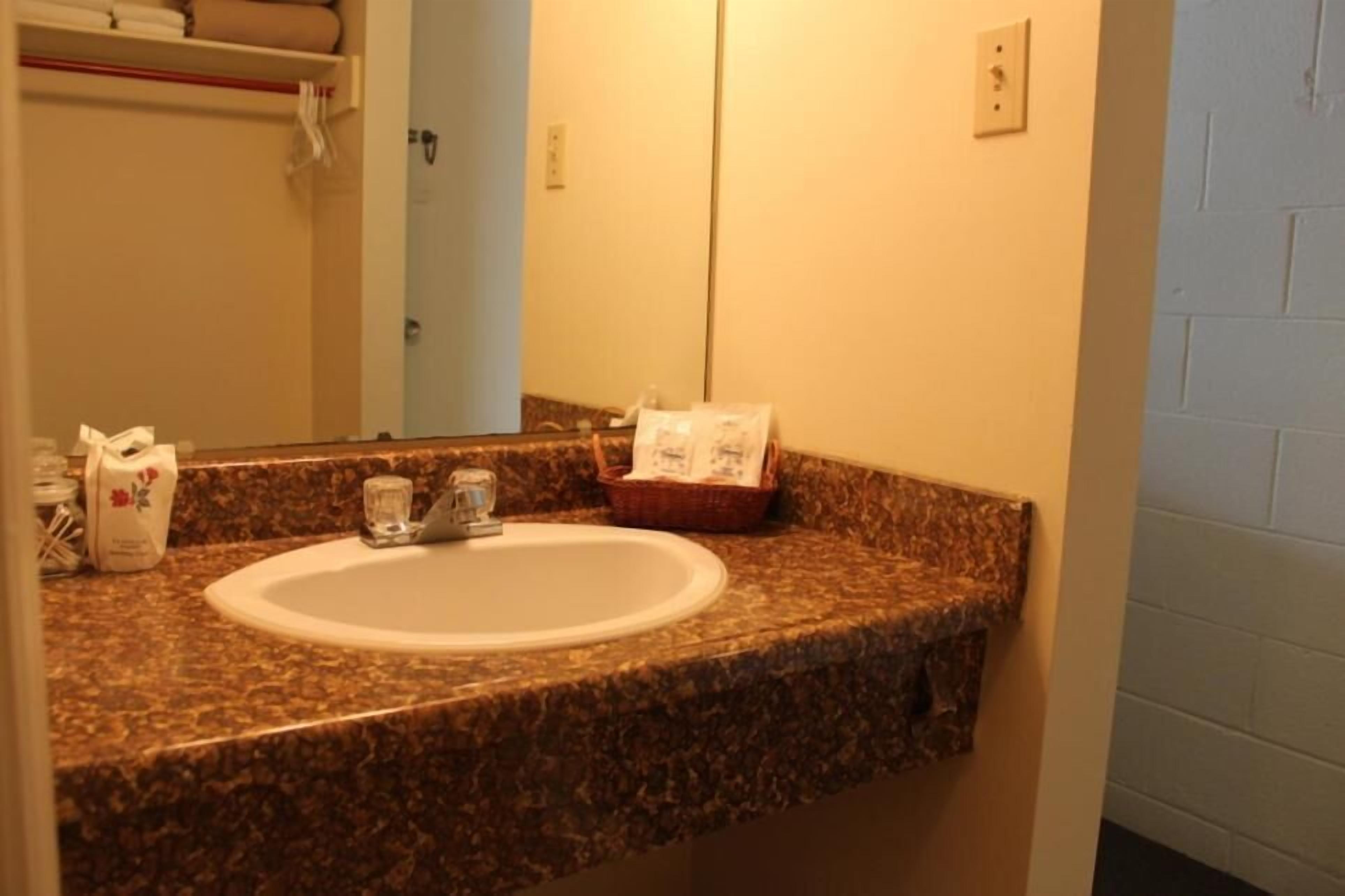 A bathroom with a granite countertop, a white sink, and a mirror. There is a basket with toiletries and a small glass on the countertop.