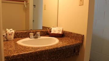 A bathroom with a granite countertop, a white sink, and a mirror. There is a basket with toiletries and a small glass on the countertop.