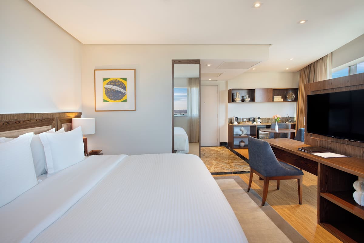 Hotelkamer met een groot bed, een bureau, een televisie en een keukenruimte zichtbaar door een geopende deur.