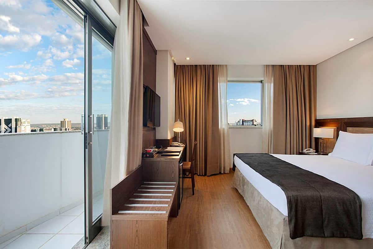 Een hotelkamer met een bed, een bureau met stoel, een televisie en uitzicht op de stad.