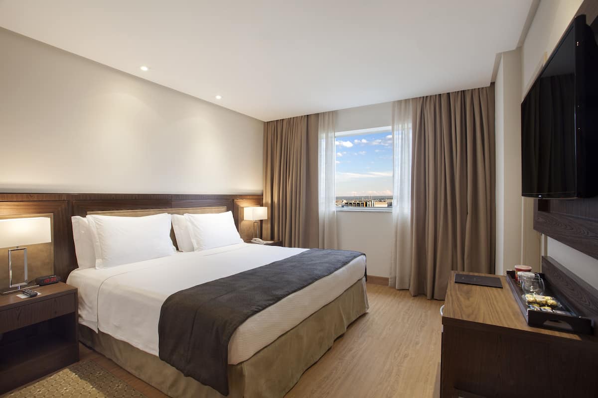 Een hotelkamer met een groot bed, bedlampen, een flatscreen-tv en een raam met gordijnen.