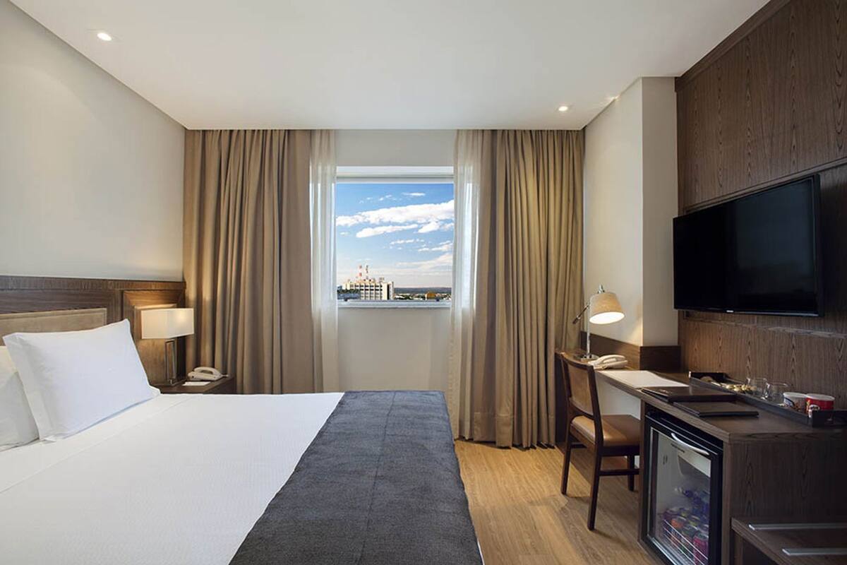 Hotelkamer met een bed, bureau, stoel, televisie en raam met uitzicht op een stadsgezicht.