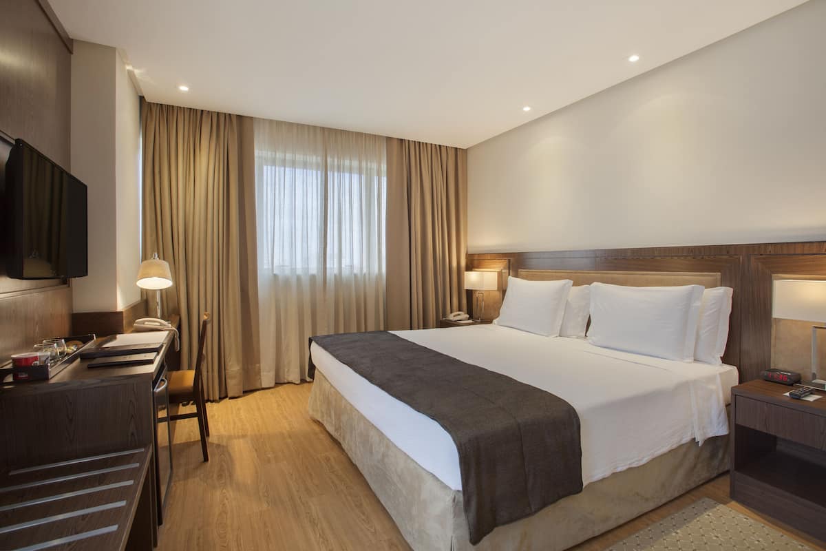 Een hotelkamer met een groot bed, een bureau met stoel, een televisie en een raam met gordijnen.