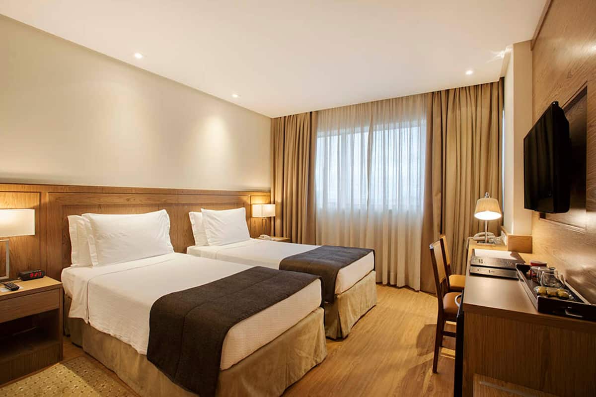 Een hotelkamer met twee bedden, een bureau, een stoel, een televisie en een raam met gordijnen.