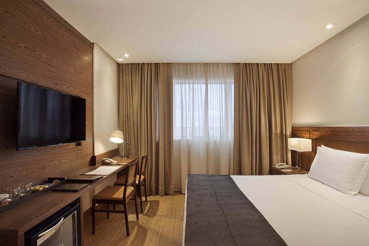Een hotelkamer met een bed, bureau, televisie en gordijnen.