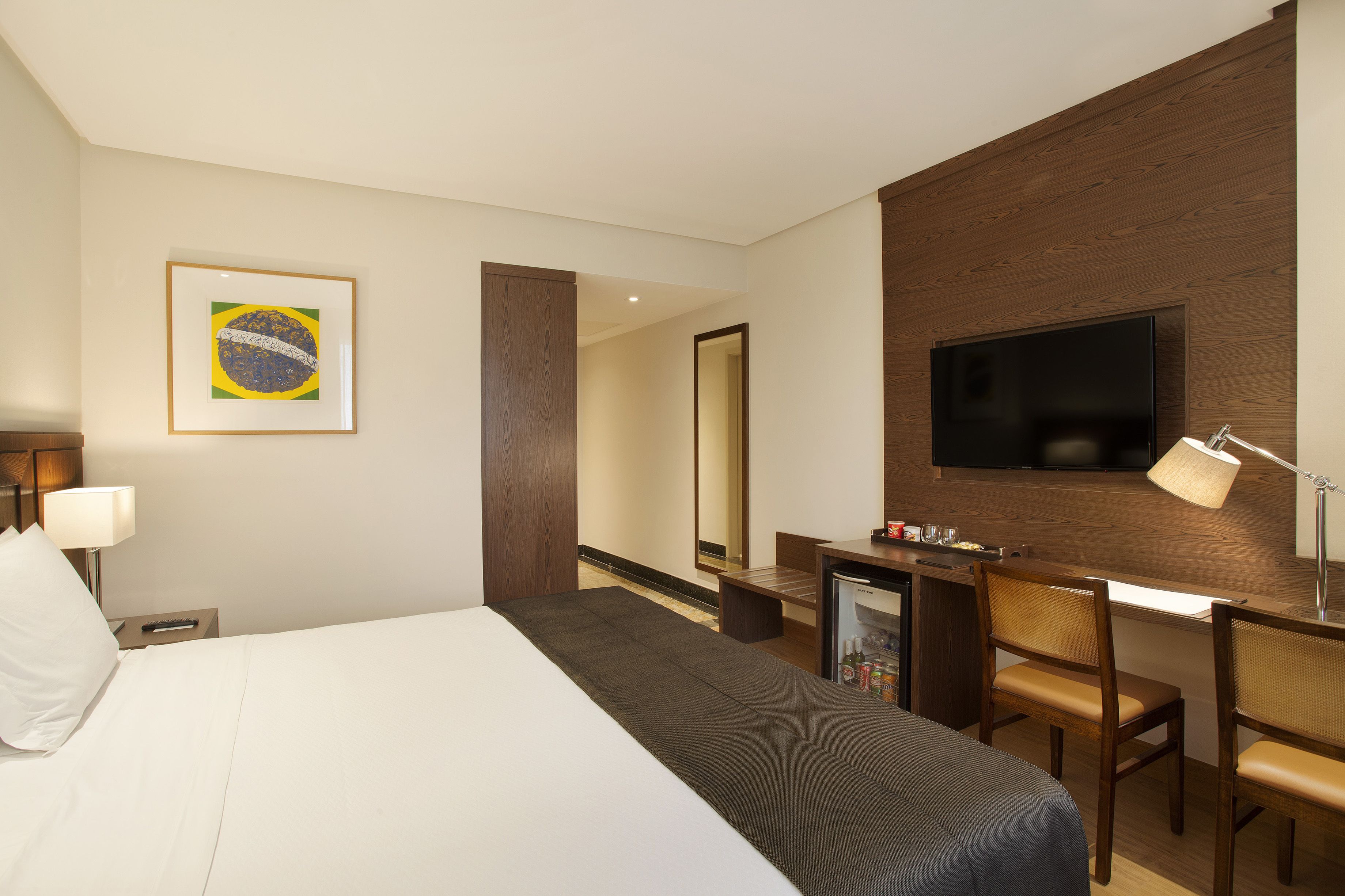 Una habitación de hotel con cama, escritorio, televisor y espejo.