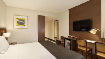 Una habitación de hotel con cama, escritorio, televisor y espejo.