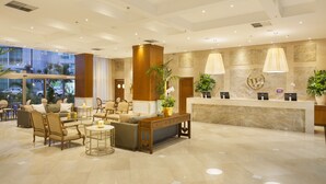 Een hotel lobby met een receptiebalie, een zithoek en grote ramen.