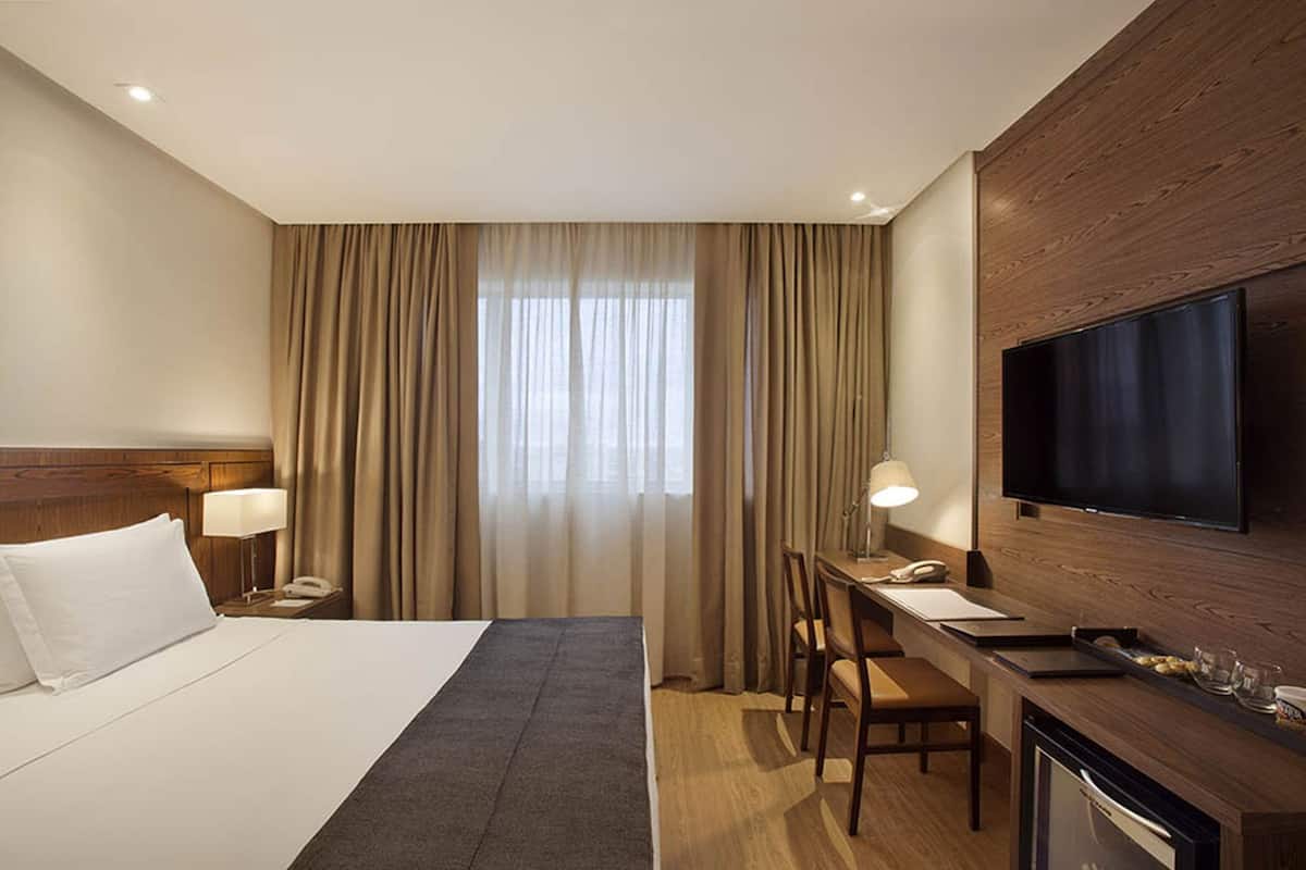 Een hotelkamer met een bed, bureau, televisie en gordijnen.