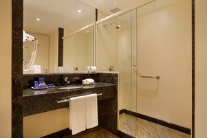 Un baño moderno con ducha de vidrio, lavamanos de mármol y un espejo grande.