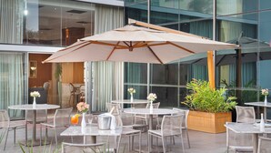 Een terras met tafels en stoelen, omgeven door potplanten en een grote parasol.
