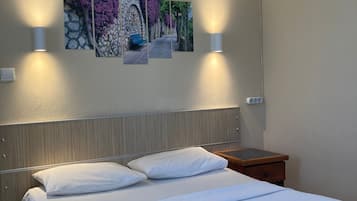 A hotel room with a bed, two wall-mounted lamps, an air conditioner, and three framed pictures on the wall.
