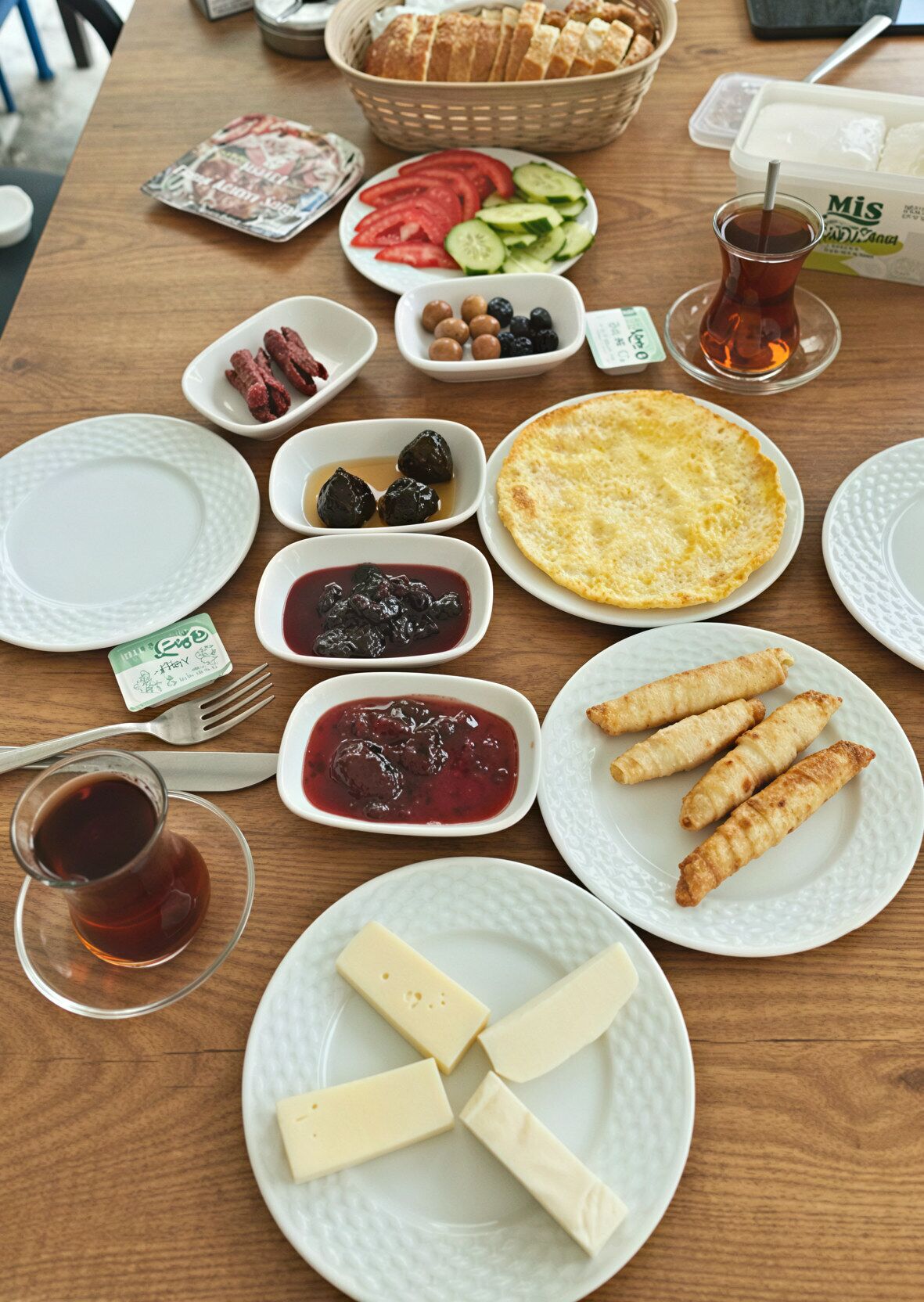 A table with various food items including bread, tomatoes, cucumbers, olives, and cheese.