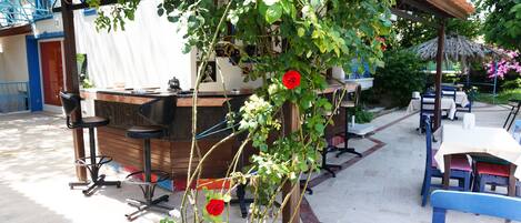 Um café ao ar livre com pérgola de madeira, balcão de bar e área de estar.