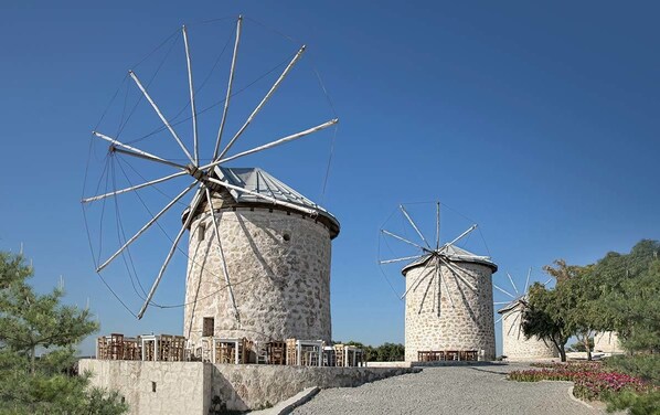 Two stone windmills with wooden sails, surrounded by buildings and trees. - Koz Marigold Apart Hotel (Cesme)