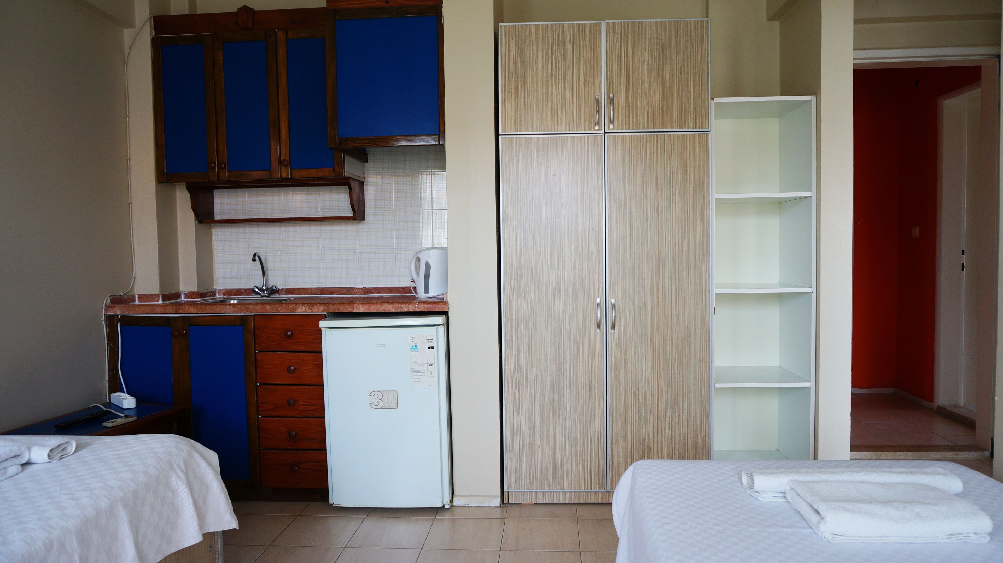 A compact hotel room with a kitchenette, a single bed, a wardrobe, and a bathroom.
