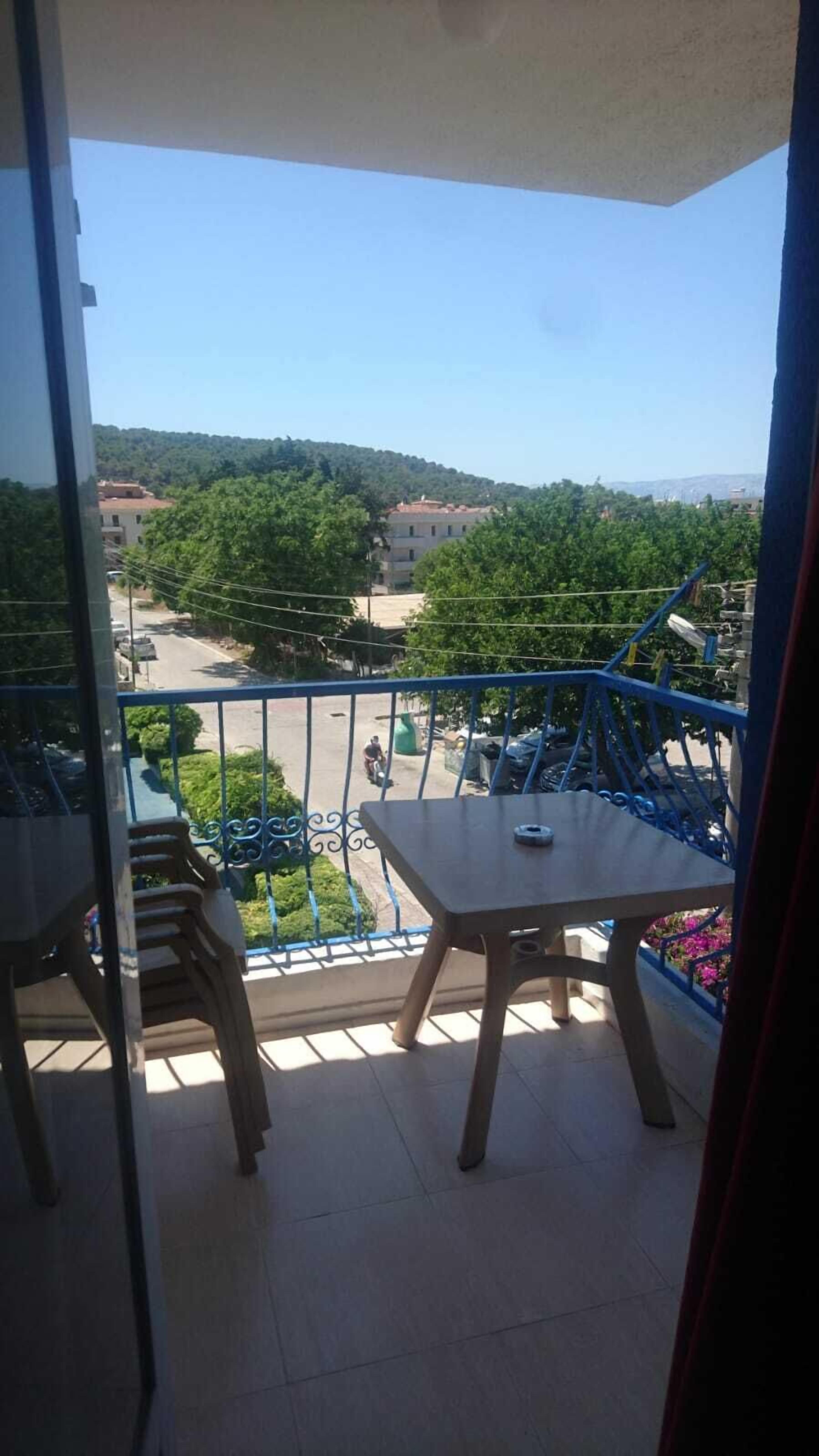 A balcony with a table and chairs, overlooking a street with parked cars and buildings.