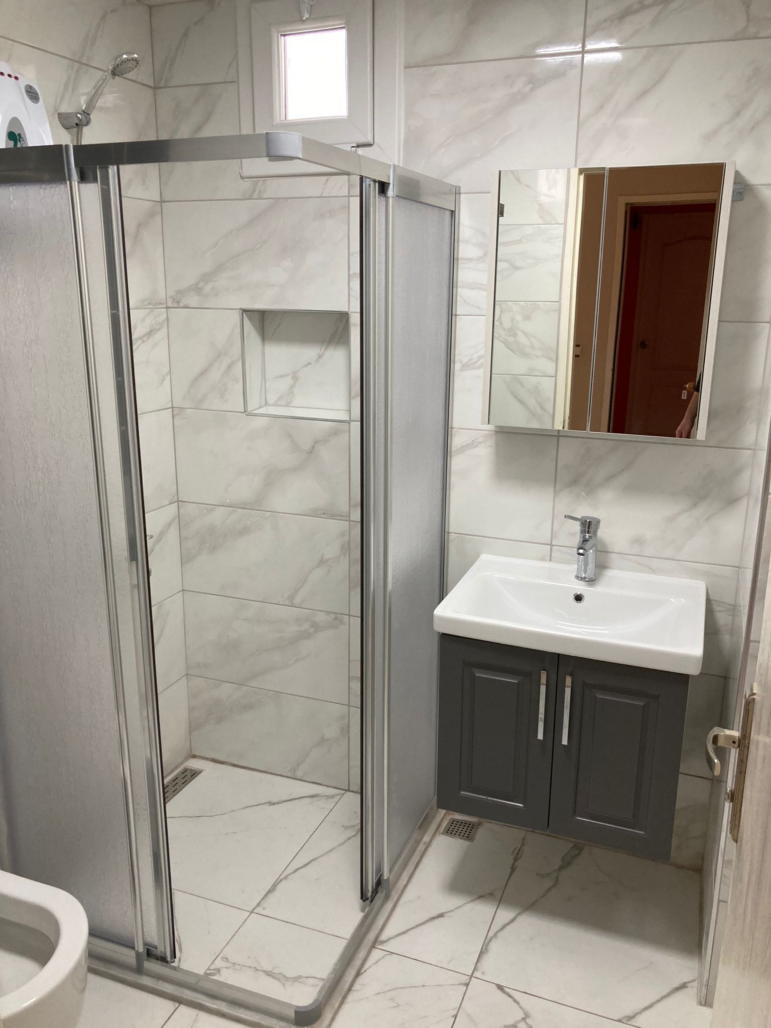 A bathroom with a glass-enclosed shower, a sink with a mirror above it, and a toilet.