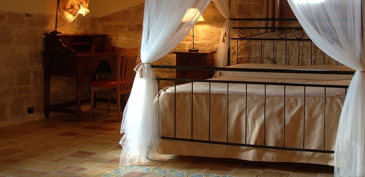 A bedroom with a four-poster bed, a wooden nightstand, a chair, and a lamp.
