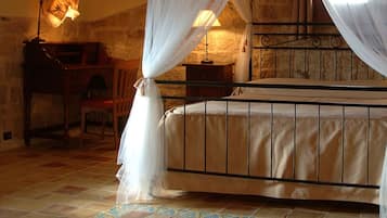 A bedroom with a four-poster bed, a wooden nightstand, a chair, and a lamp.