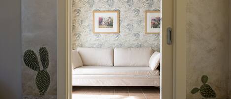 A room with a beige sofa, patterned wallpaper, and cactus artwork on the walls.