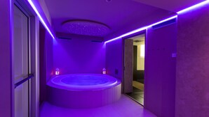 Un baño moderno con una bañera de hidromasaje circular central, iluminación ambiental morada y un diseño de techo con motivos de estrellas.