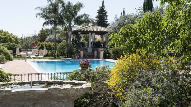 Zona de piscina con muro de piedra, sillas de descanso y un pabellón.