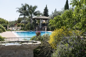 A pool area with a stone wall, lounge chairs, and a gazebo. - Agriturismo Il Granaio (Modica)