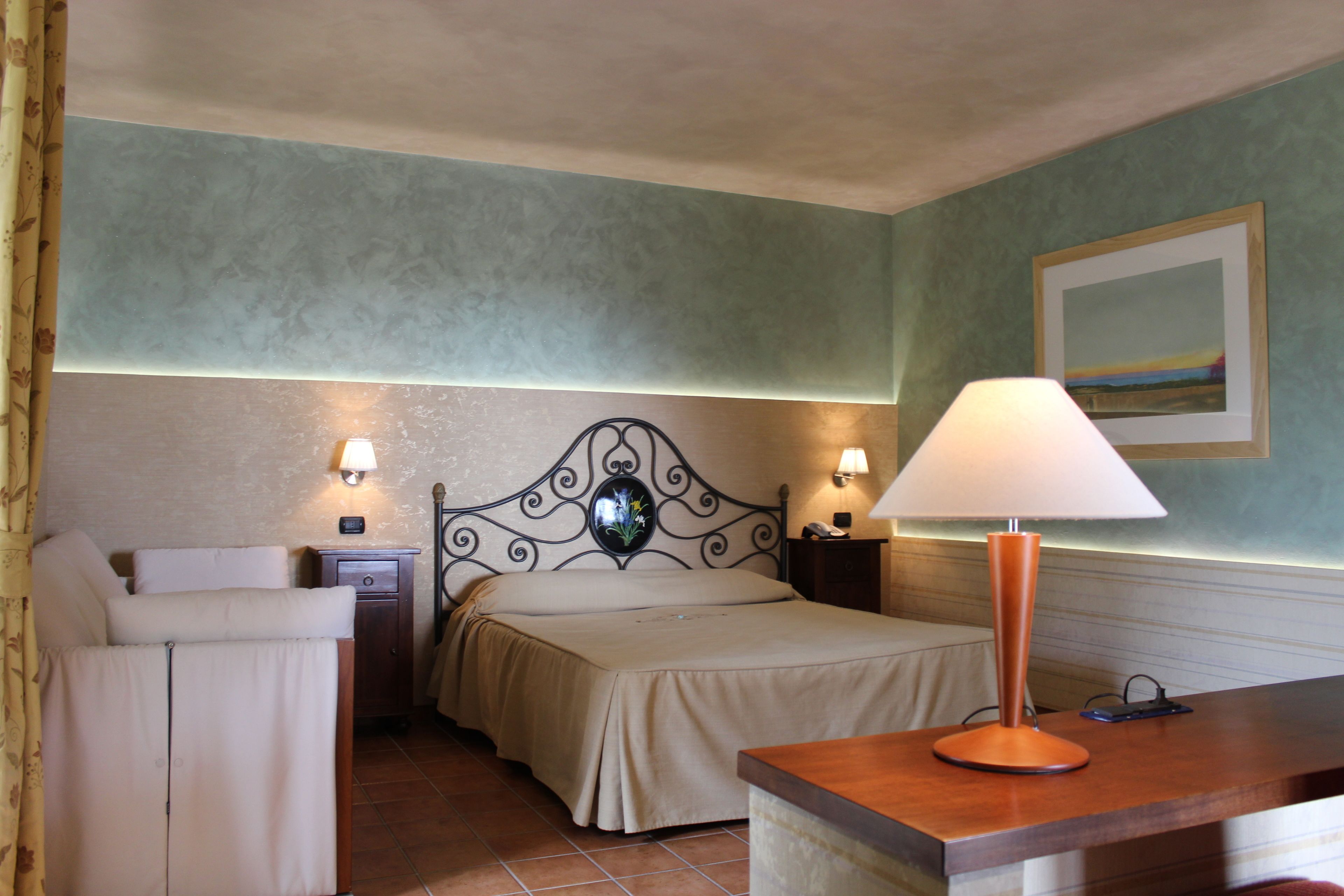 A hotel room with a bed, bedside tables, a lamp, and a painting on the wall.