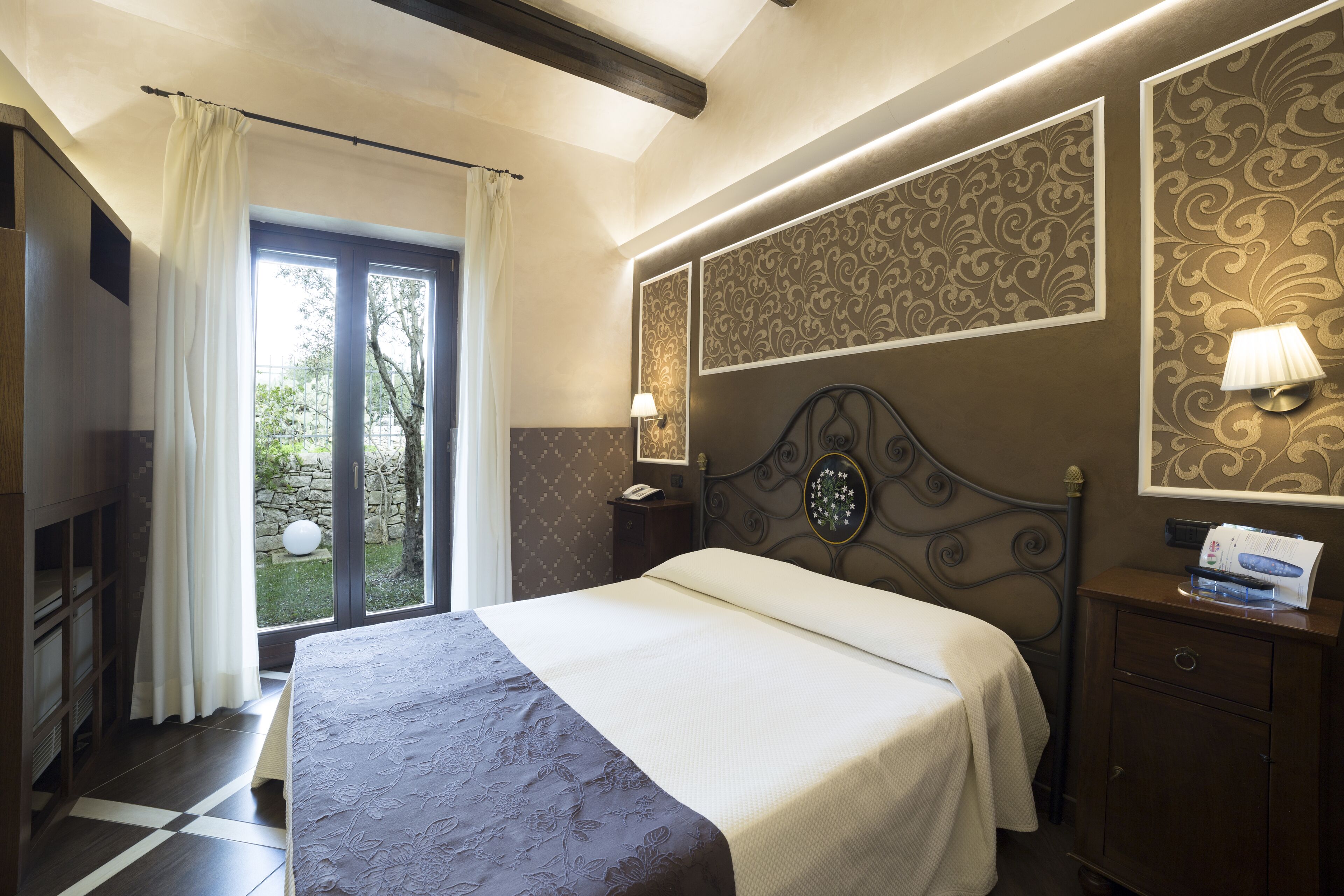 Une chambre à coucher avec un lit, une table de chevet, une lampe, une armoire et une fenêtre avec des rideaux.