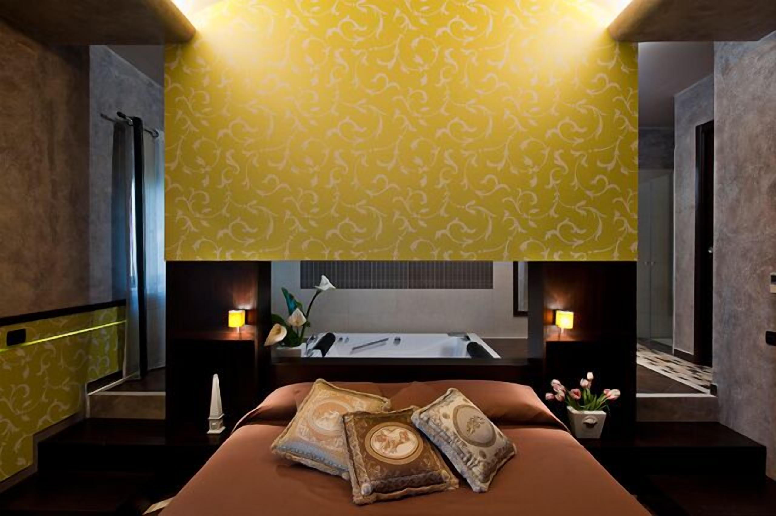 A hotel room with a large bed, two bedside lamps, a nightstand, a small table, and a potted plant.