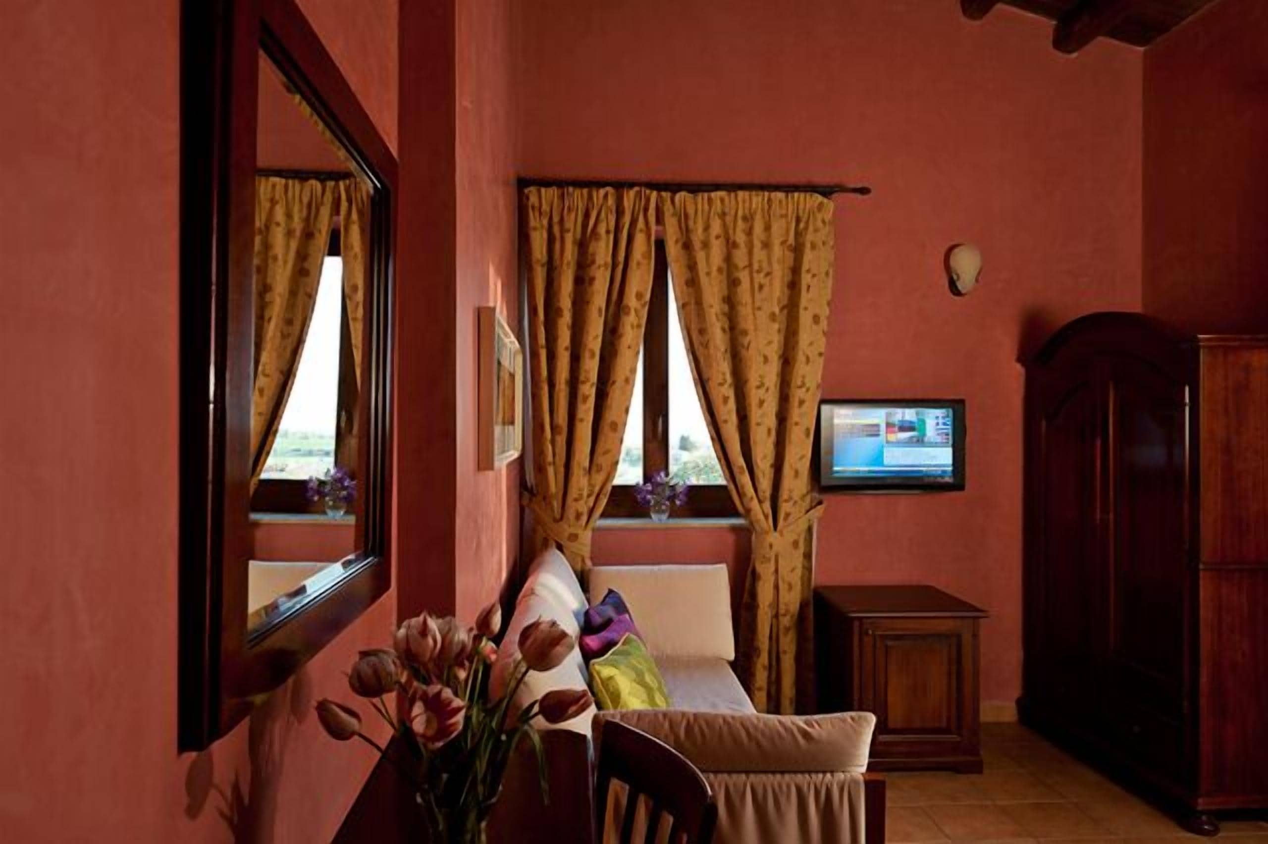 A room with a bed, a television, a wooden cabinet, and a window with curtains.