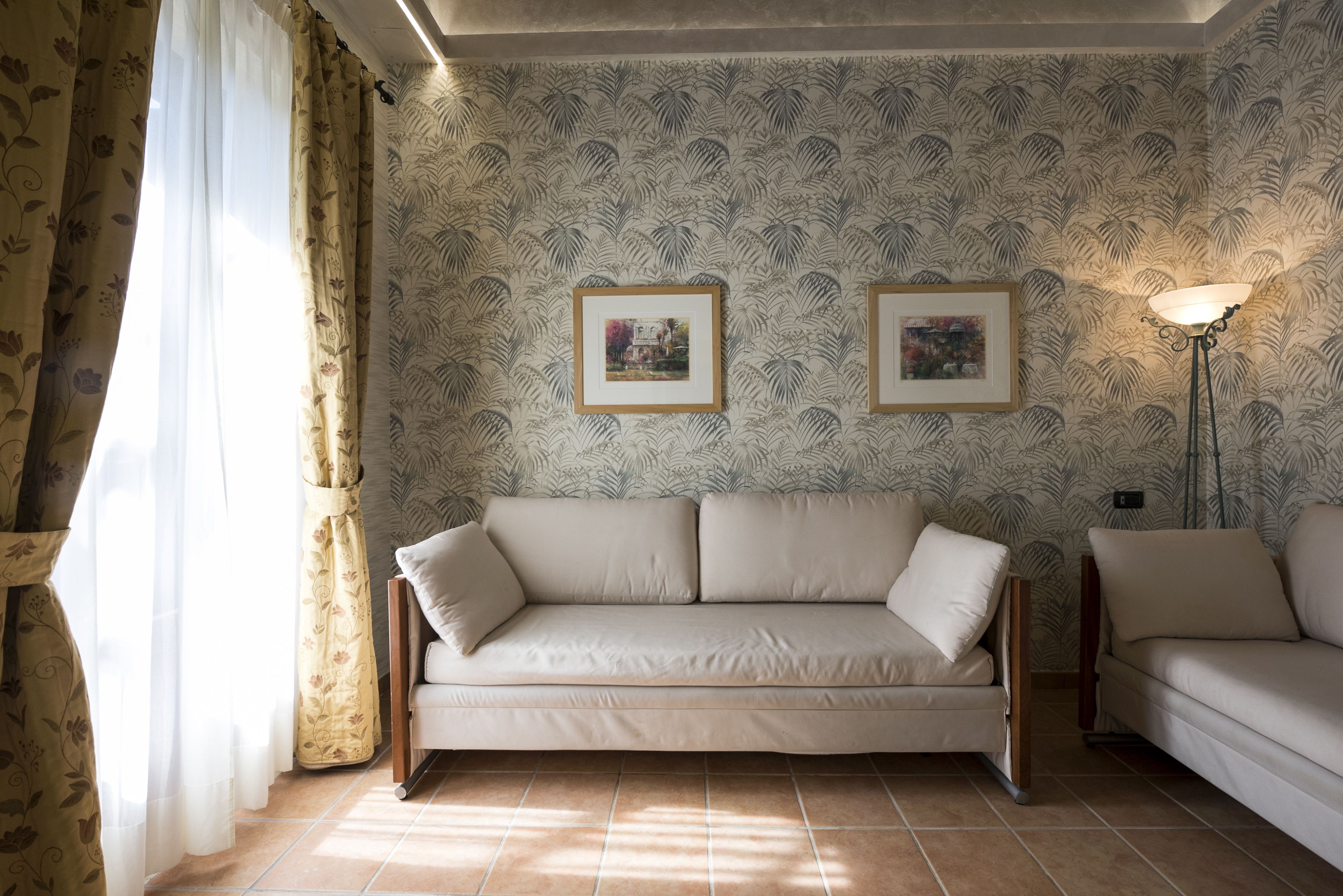 Una sala de estar con un sofá color crema, un papel tapiz estampado y dos cuadros en la pared.