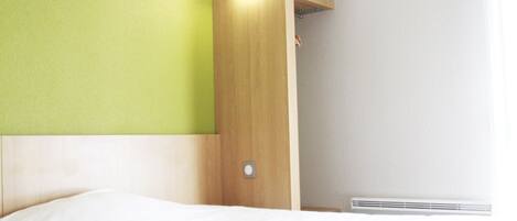 Habitación de hotel con cama, cabecera de madera, pared verde y ventana con cortinas blancas.