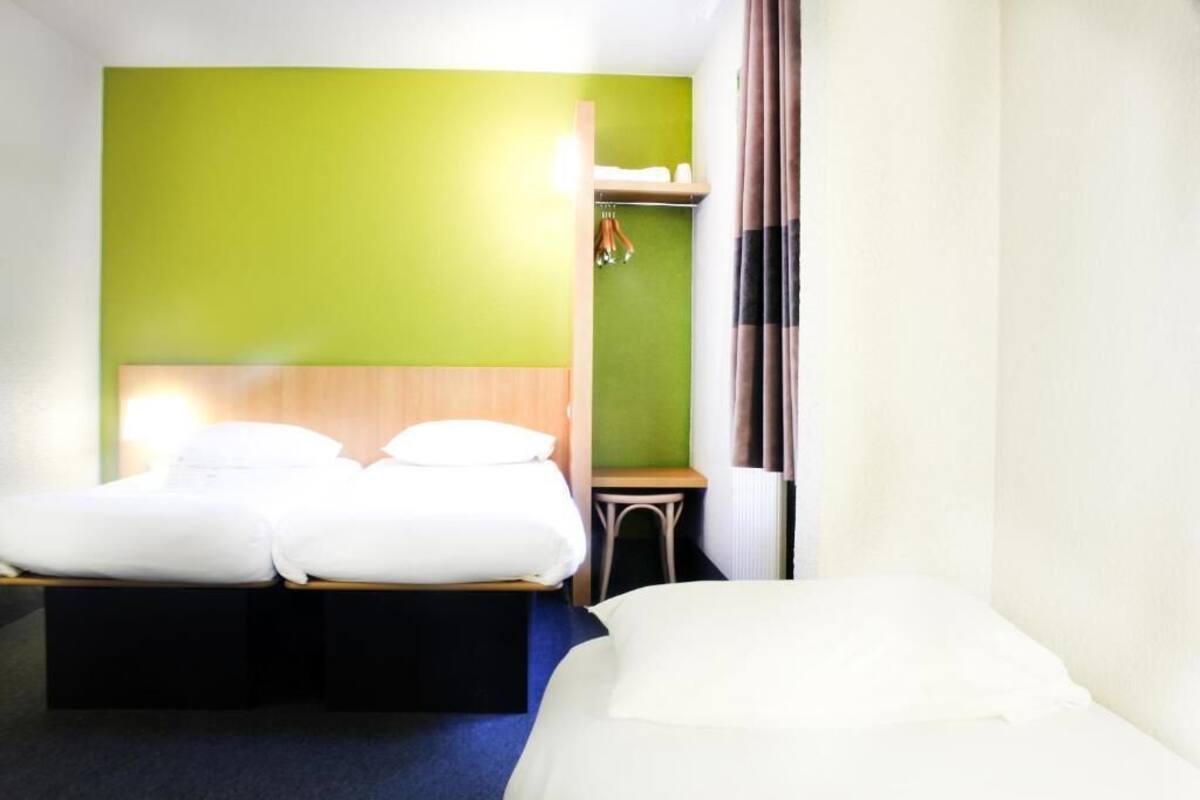 A hotel room with two beds, a small table, and a green accent wall.