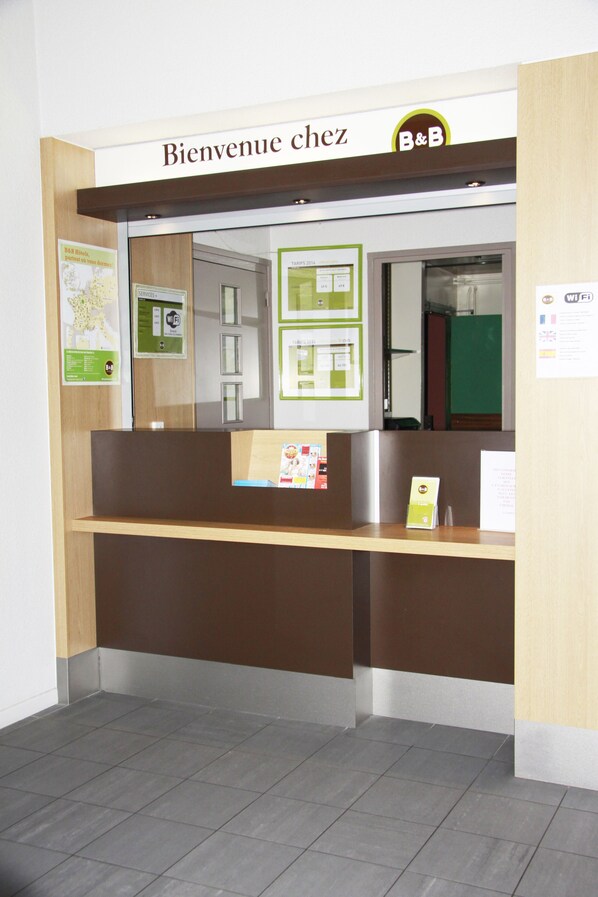 A reception desk with a sign reading "Bienvenue chez B&B" and a map on the wall. - Hôtel Inn Design Vierzon (Vierzon)