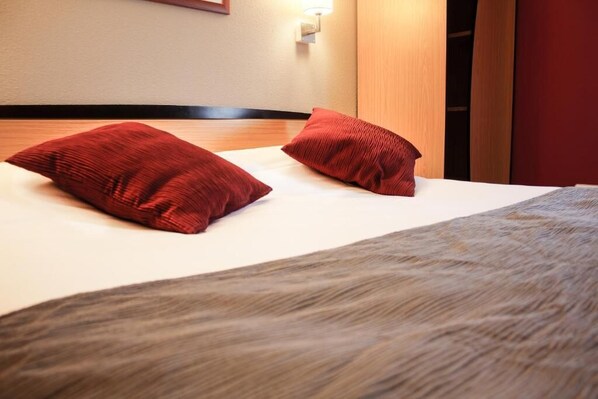 A hotel room with a bed, two red pillows, a wooden headboard, and a wall-mounted light fixture. - Hôtel Inn Design Vierzon (Vierzon)